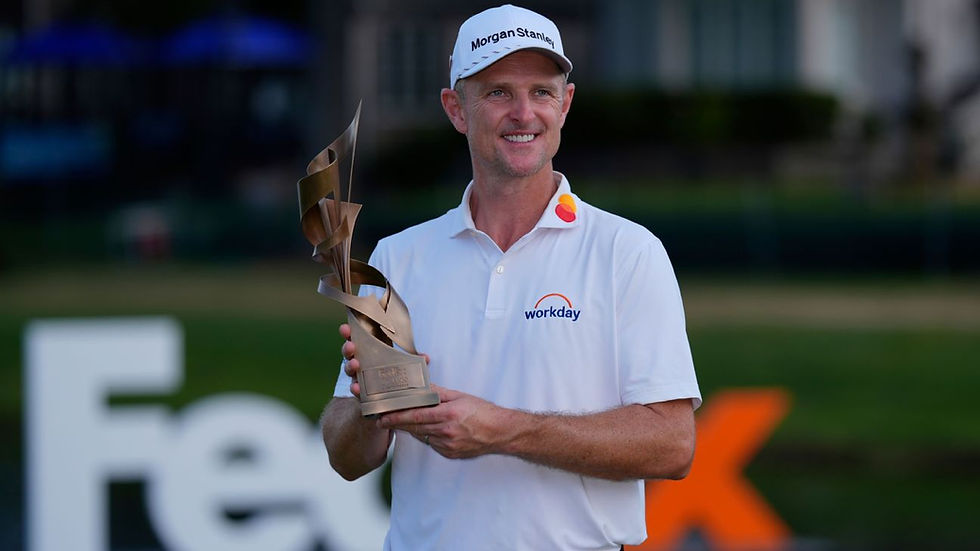 Golfer in a white polo and cap holds a bronze trophy, smiling. Logos visible on shirt. Blurred outdoor background with FedEx text.