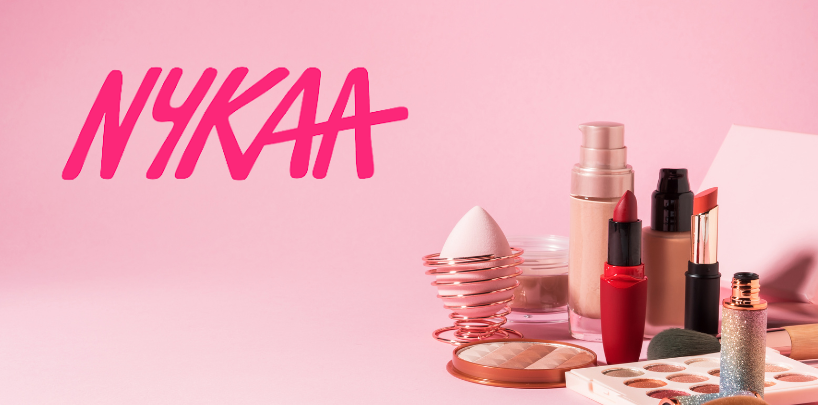 Makeup products on a pink background with "NYKAA" text in bold. Includes lipsticks, foundation, and eyeshadow, creating a stylish vibe.
