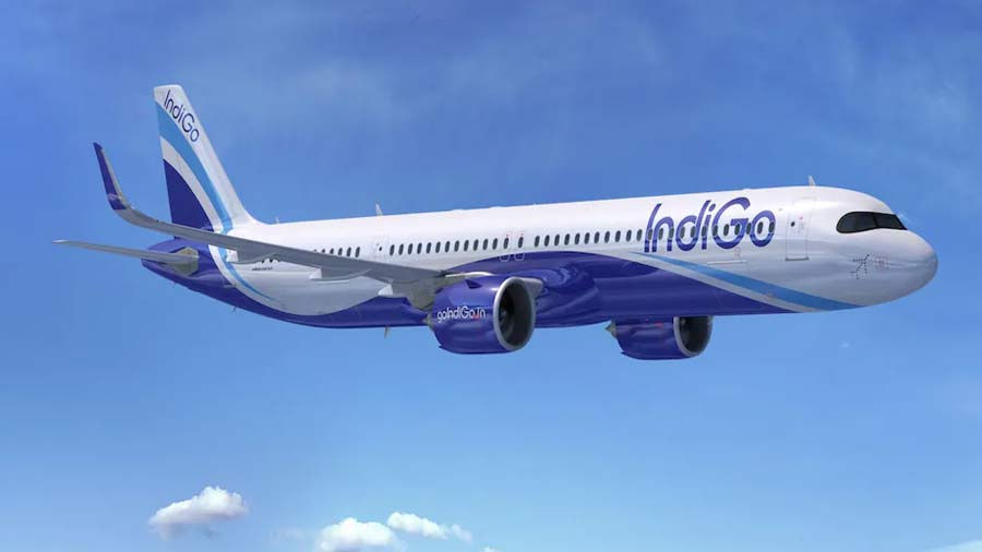 IndiGo airplane soaring in a clear blue sky. White and blue design with visible logo on the side. Few clouds below suggest altitude.