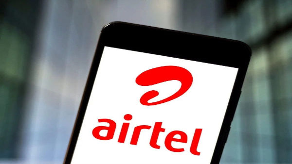 Smartphone displaying the Airtel logo in red on a white background, set against a blurred blue and gray backdrop.