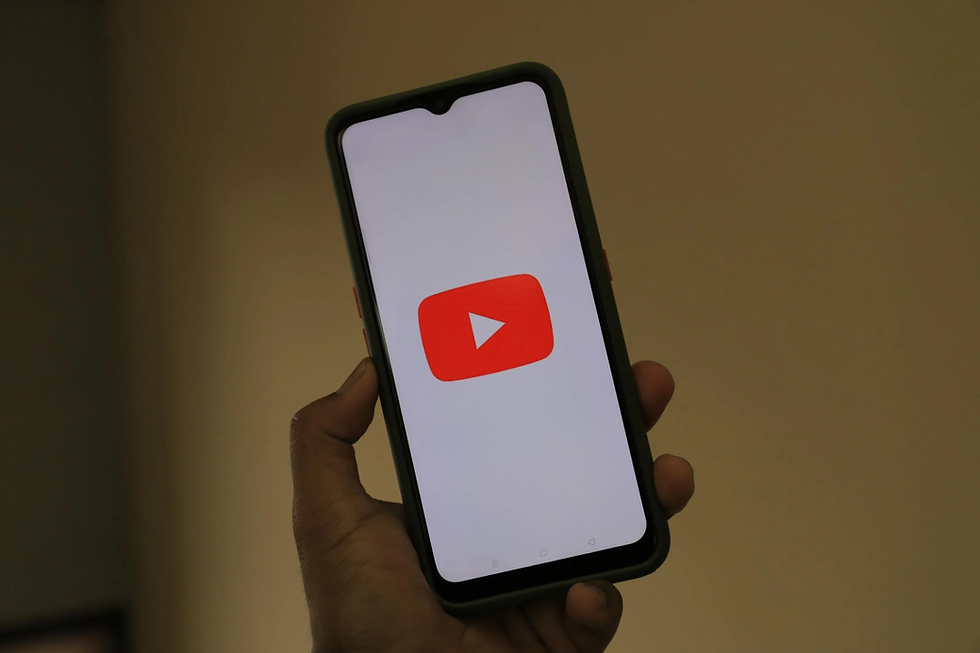 Hand holding a smartphone displaying the red YouTube logo on a white screen. The background is plain beige.