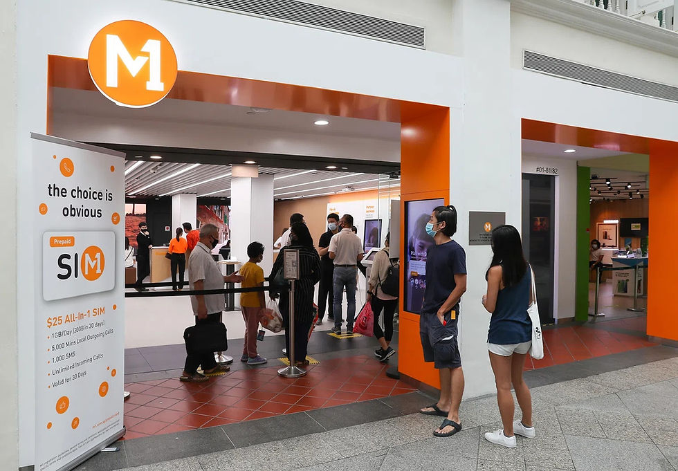 People stand in line at an M1 store. The sign reads "the choice is obvious." The interior has orange accents, creating a lively atmosphere.