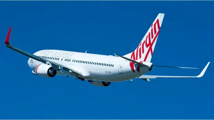 White Virgin Australia airplane in flight against a clear blue sky, featuring red branding on the tail and wings.