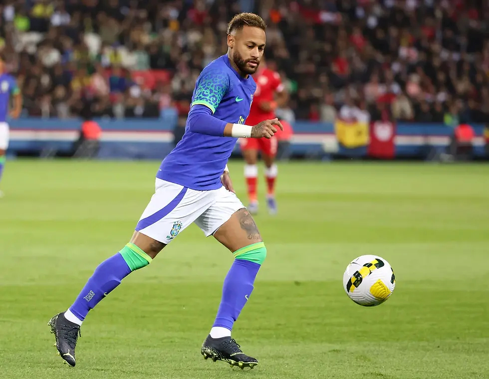 Soccer player in a blue and green jersey dribbles a ball on a green field. Crowd in the background, flags visible. Focused and intense mood.