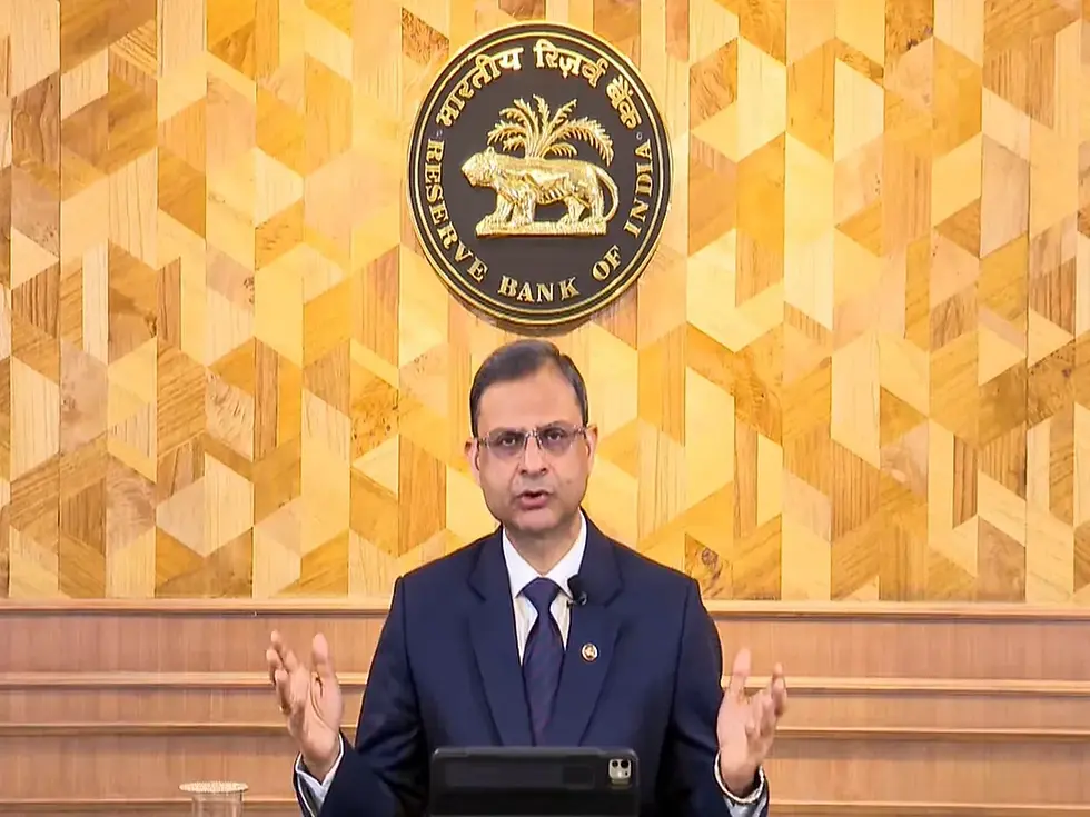 Man in a suit speaking, hands gesturing, in front of Reserve Bank of India logo. Wooden patterned background adds warmth.