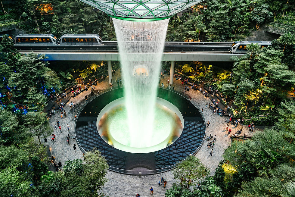 "Interior view of Singapore Changi Airport's Jewel, showcasing the world's tallest indoor waterfall surrounded by lush greenery, creating a tranquil and luxurious environment for travelers."