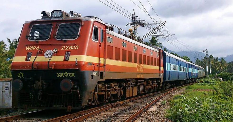Red and blue train with "WAP4 22820" on tracks, lush greenery around, overhead wires visible, cloudy sky in the background.
