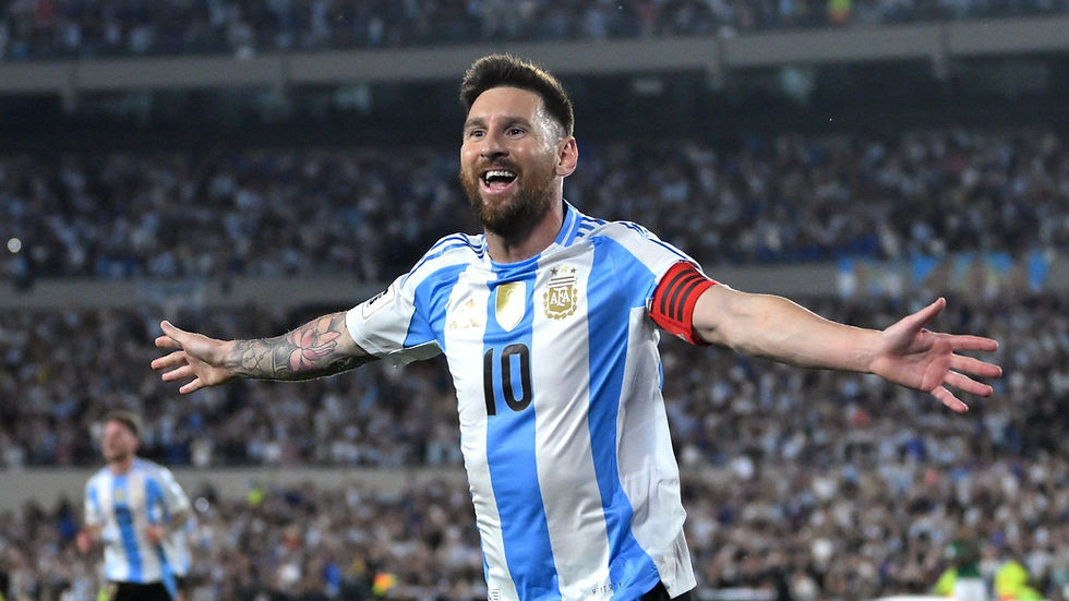 Soccer player in blue and white jersey with a red armband celebrates on a crowded stadium field, arms outstretched, smiling joyfully.