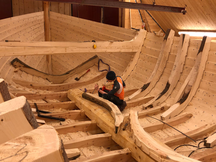 Ein klinkbåt under oppføring på modulkurset Trebåtbyggar ved Museet Kystens Arv. Ein deltakar jobbar midt i båten.