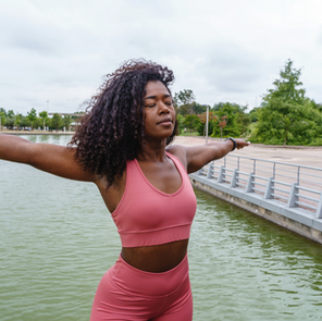 Black woman standing near a lake with arms extended and eyes closed.