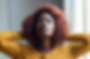 Black woman with red natural hairstyle and yellow shirt with hands at head looking like she's destressing.