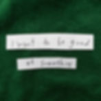 "I want to be good at something" hand printed on 2 strips of white paper with black sharpie, and placed on some dark green material. 