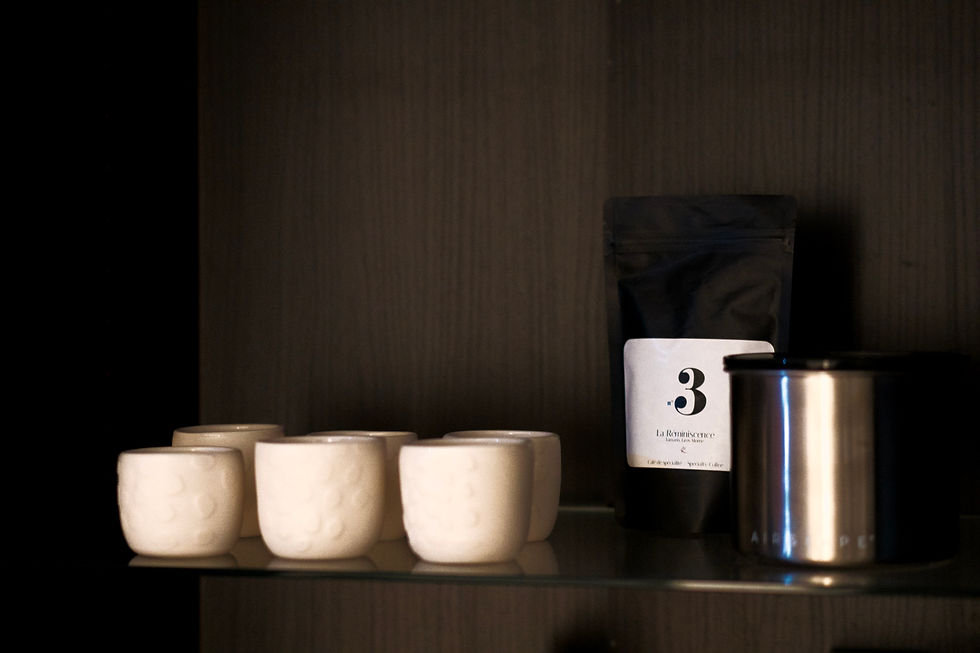 Étagère sombre avec cinq tasses crème, un sachet de café noir marqué n°3 La Réminiscence et un pot métal.