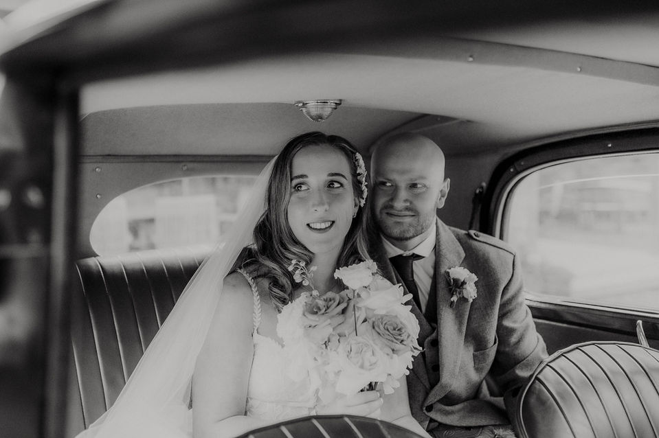 Bride and groom in a vintage car smiling at Broxmouth Courtyard photographed by Karol Makula.