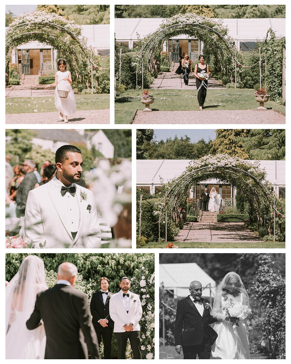 Bride walks down aisle under floral archway in a garden, accompanied by a man. A groom in a white tux waits, smiling amid guests.