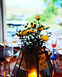 En vas med gula blommor står på ett uppdukat bord utomhus
