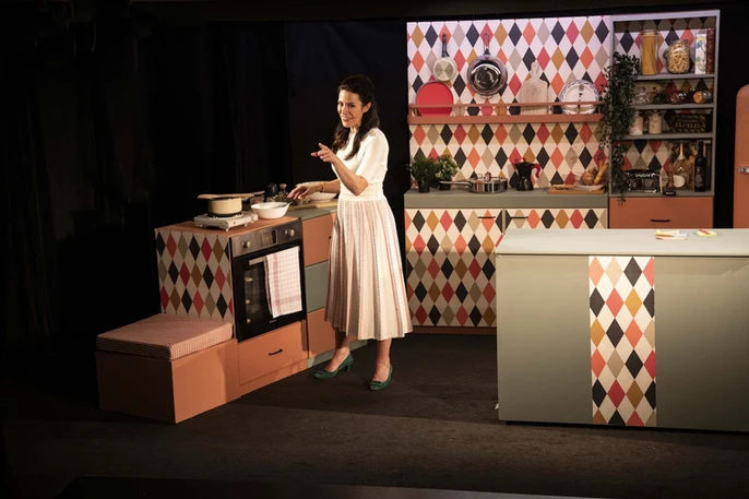 Image de "Dévorante" avec Eleonora Galasso à côté d'un four rétro, en pleine conversation ou récit, dans un décor de cuisine qui reflète l'élégance et le charme italien.