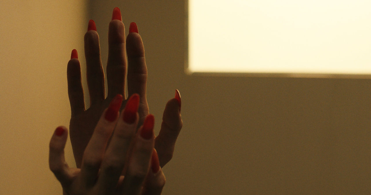 Les mains aux ongles peints de rouge vif s'entrelacent dans une gestuelle qui suggère un moment de connexion profonde, capturé dans 'Boléro'.