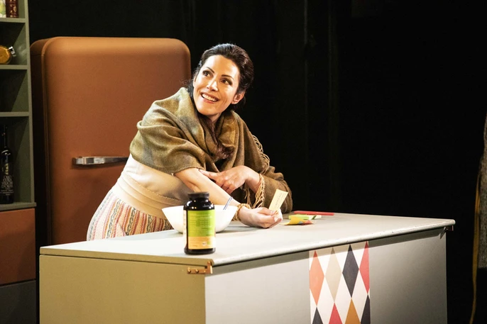 Eleonora Galasso dans "Dévorante", souriante, accoudée à une table de cuisine rétro, prépare des ingrédients avec attention, évoquant chaleur et convivialité.