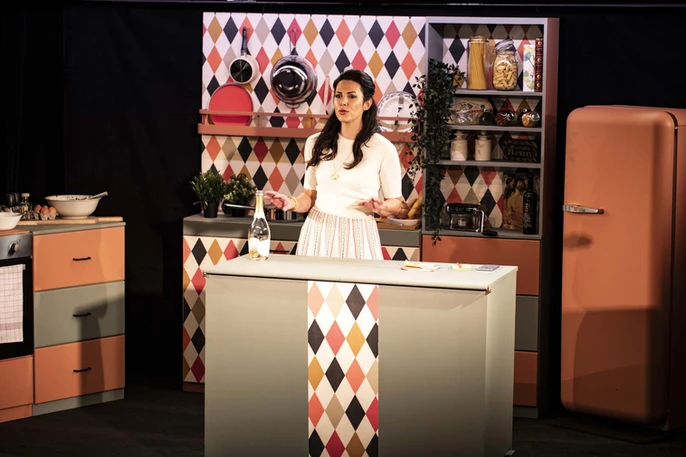 Scène de "Dévorante" montrant Eleonora Galasso dans une cuisine colorée et stylisée, incarnant un personnage en pleine démonstration culinaire, capturant l'essence de la Dolce Vita.