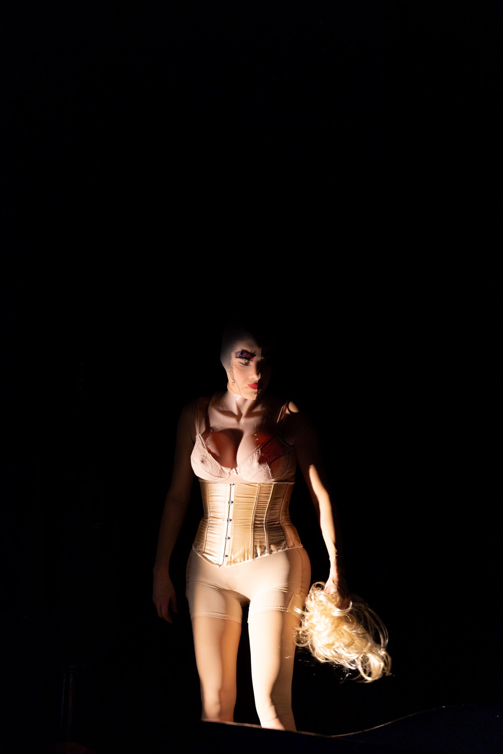 Une scène de 'Ex Machina' présentant une interprète en corset, éclairée de manière dramatique sur le côté contre un fond noir.