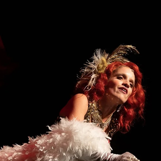 Actrice en tenue de cabaret : Une actrice en costume de cabaret, avec des plumes blanches et une coiffure extravagante, interprète un rôle sur scène.