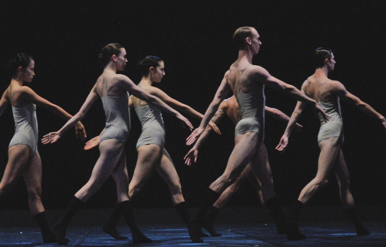 Une chaîne humaine de danseurs de 'Love Chapter 2' se déplaçant avec une précision mécanique, une représentation de la complexité des relations humaines.