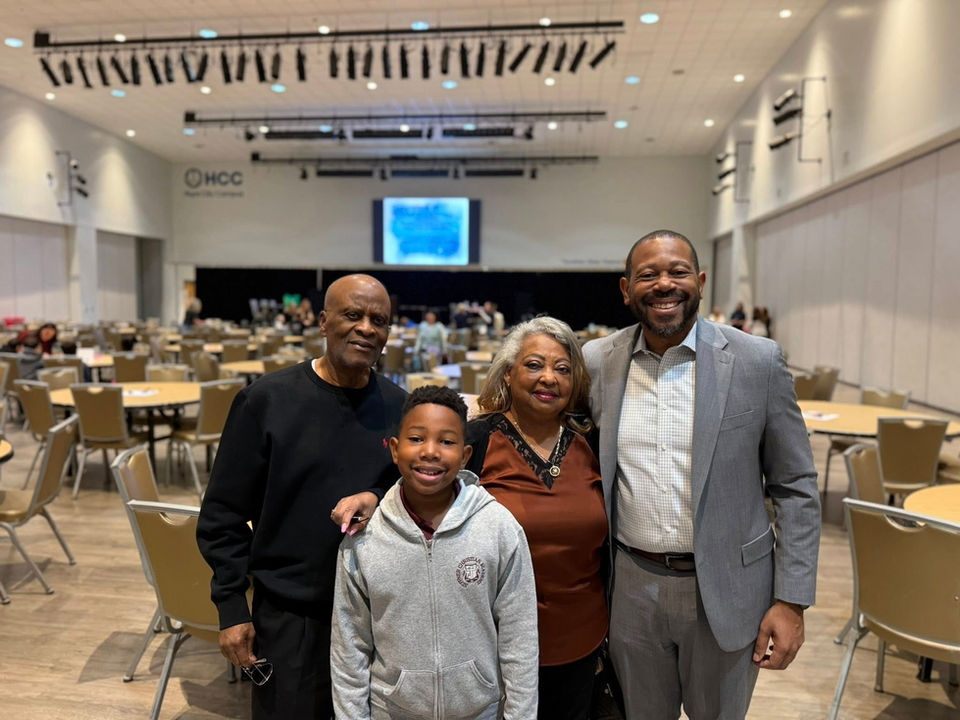 Four smiling family members pose happily together in a large event hall.