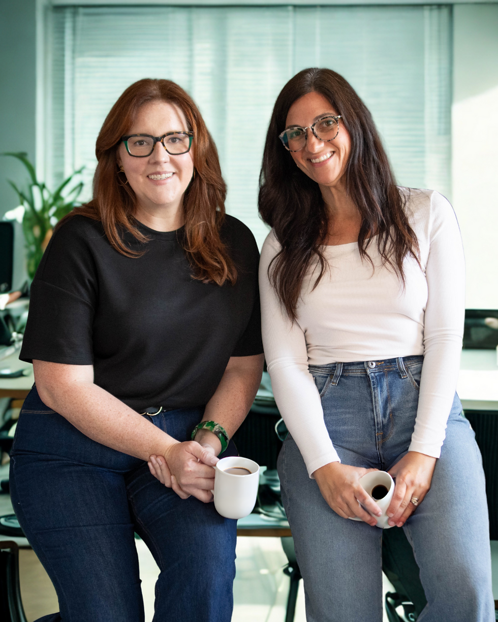 Kelly and Joann sitting on an office desk drinking luke warm coffee