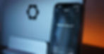 Smartphone displaying "What can I help with?" in front of a laptop with a gear icon. The background has a warm orange glow.