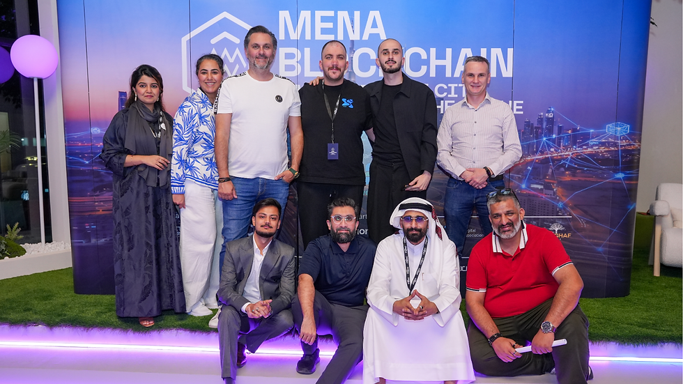 Group of nine posing at MENA Blockchain event, smiling before blue cityscape backdrop with LED glow and event text.