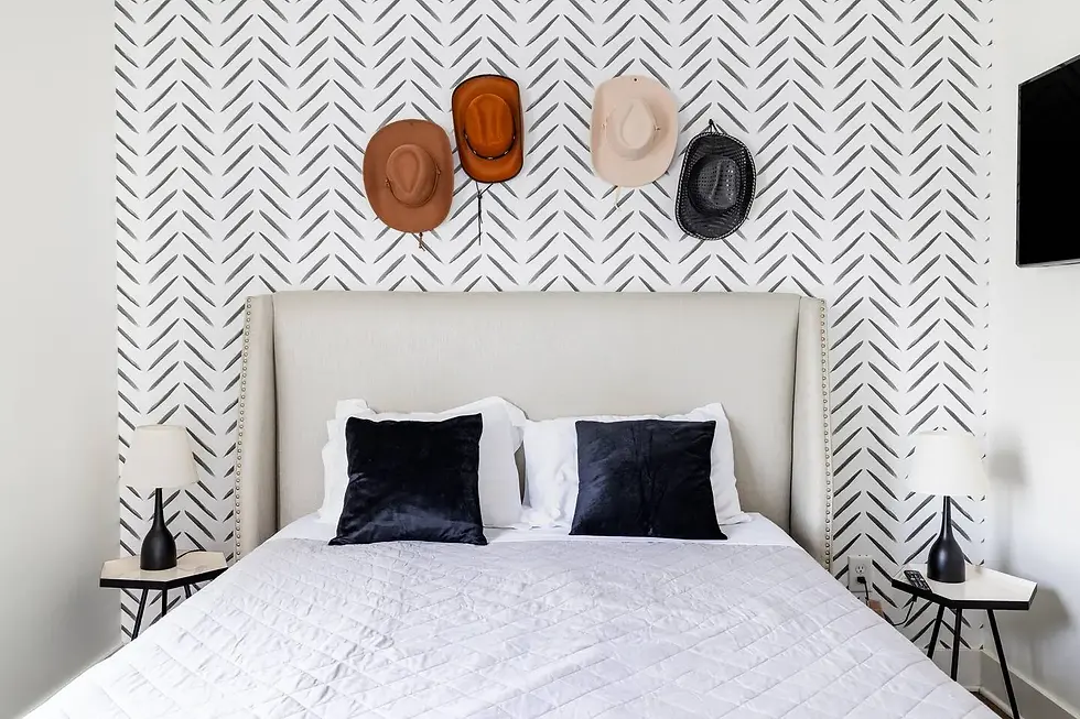 Modern bedroom with herringbone accent wall, upholstered headboard, and cowboy hat decor at Nashville couple's retreat