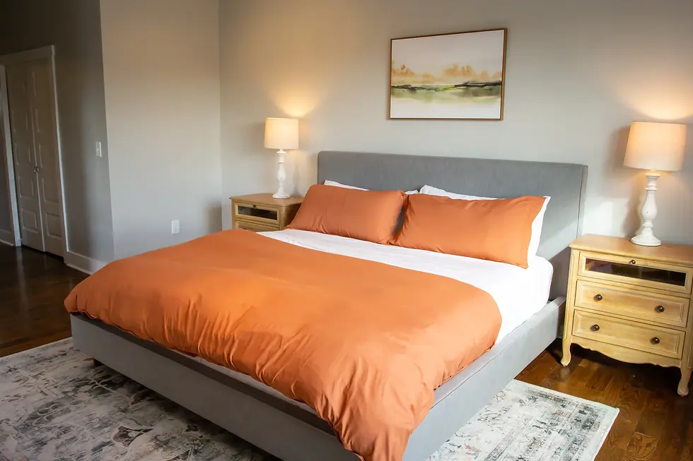 Modern master bedroom with gray upholstered bed and orange bedding at Underwood Manor, a Tennessee countryside retreat