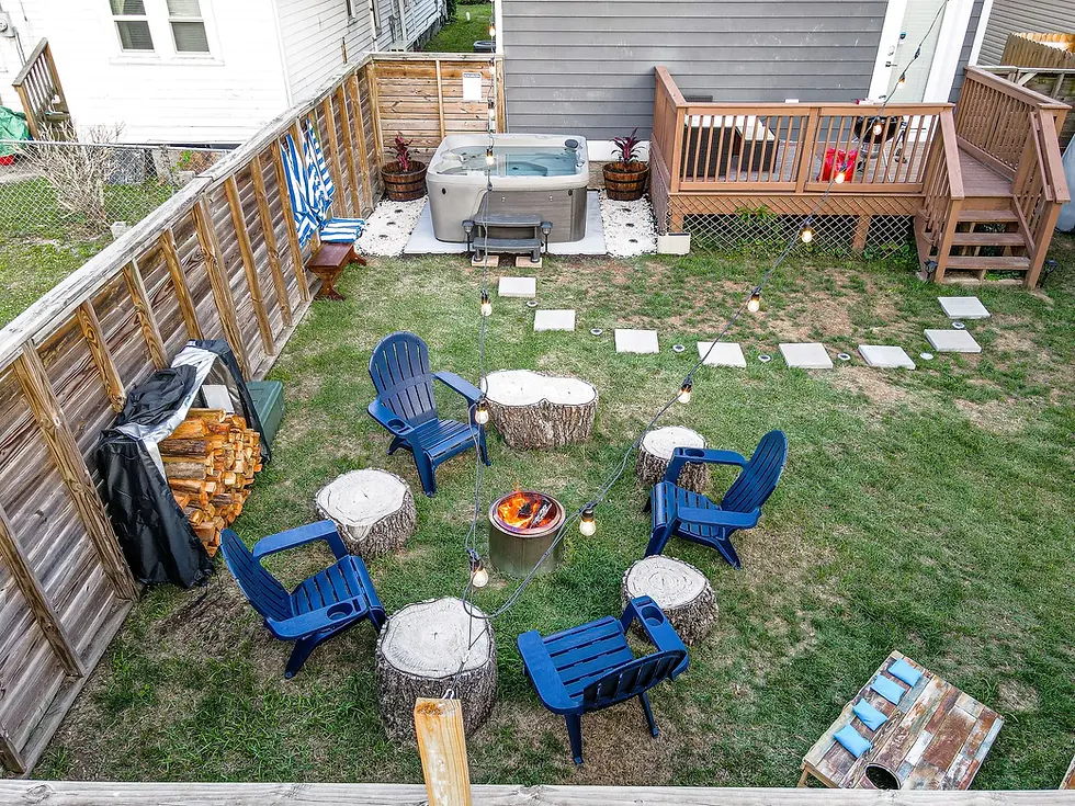 Backyard patio with hot tub, fire pit, and Adirondack chairs surrounded by manicured lawn and wooden decking