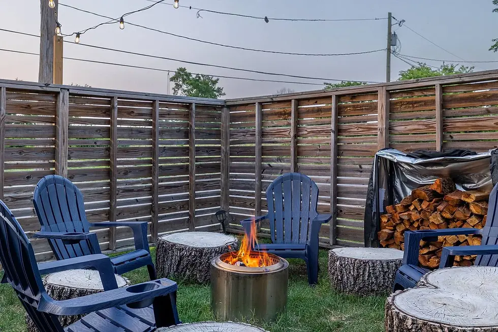 Fire pit with blue Adirondack chairs, log seating, and stacked firewood on a patio for a hot tub and fire pit winter trip in