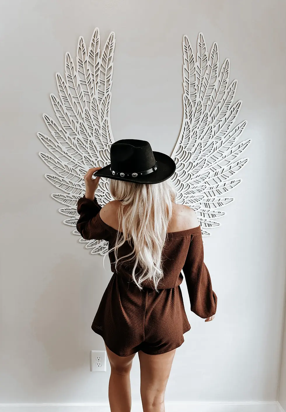 Woman in brown off-shoulder top and black cowboy hat poses against white feathered wing wall art at Nashville Tennessee