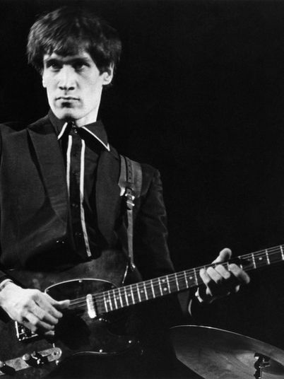 Wilko Johnson of Dr. Feelgood performs live during the 1970s pub rock era, playing electric guitar on stage in a black-and-white concert photograph.