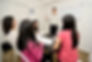 A teacher is teaching four female students in a small room. The students have their books on top of a black table.