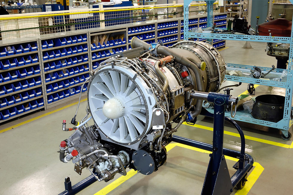 Jet engine on a stand in an industrial workshop. Blue shelves in the background hold small parts. Bright lighting, organized setting.