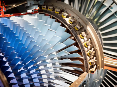 Close-up of a jet engine turbine with blue and silver blades. The intricate fan design creates a dynamic, industrial feel.