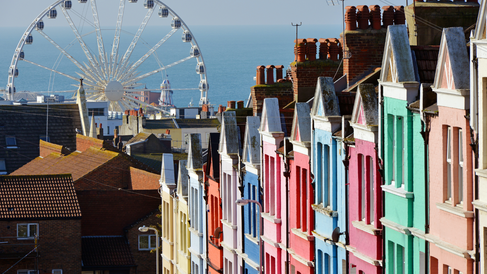 vista panoramica de brighton con casas en fila de colores rosa verde y azul y una rueda de la fortuna en el fondo delante del mar en inglaterra