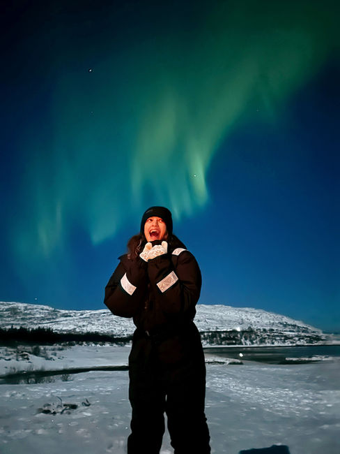 mujer joven vestida con traje termico en el artico con auroras boreales verde grandes en el cielo en tromso noruega