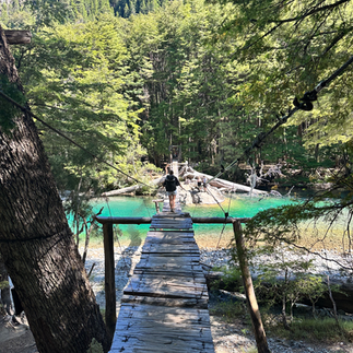 mujer cruzando un puente de tablas de madera rustico sobre un rio cristalino traslucido en el cajon del azul en el bolson argentina