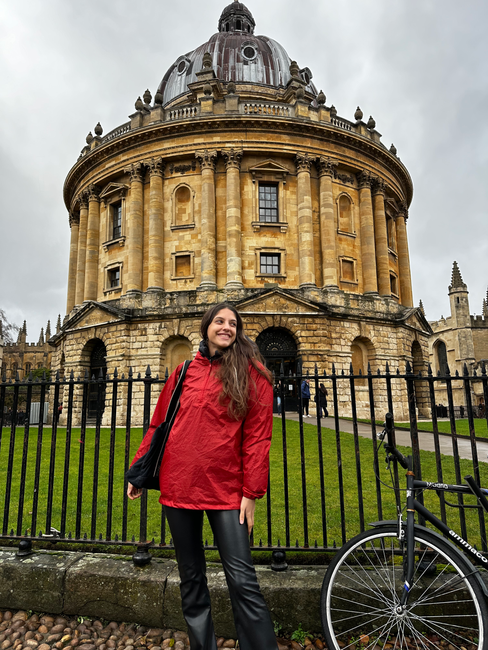 mujer joven con poncho de lluvia rojo en oxford inglaterra frente a la libreria Bodleian