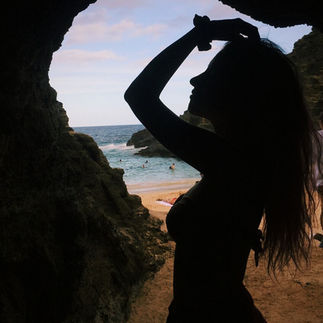 mujer de perfil con la sombra de su silueta en una cueva con salida a la playa y el mar en hawaii