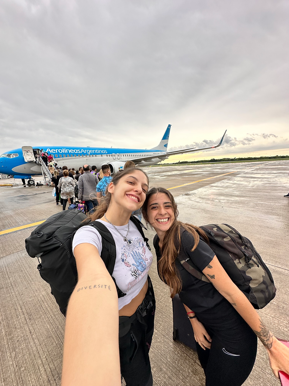 dos mujeres jovenes amigas mochileras delante de un avion de aerolineas argentinas camino a bariloche y al cajon del azul en el bolson argentina