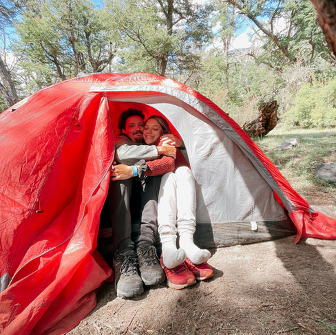 pareja joven abrazandose felices dentro de una carpa roja haciendo camping agreste en un bosque de patagonia argentina en camino de los 7 lagos