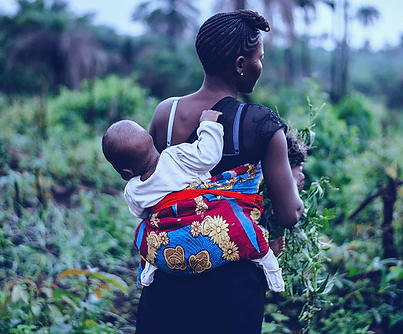 A mother is carrying her child in a back pack, as she works to gather greens.