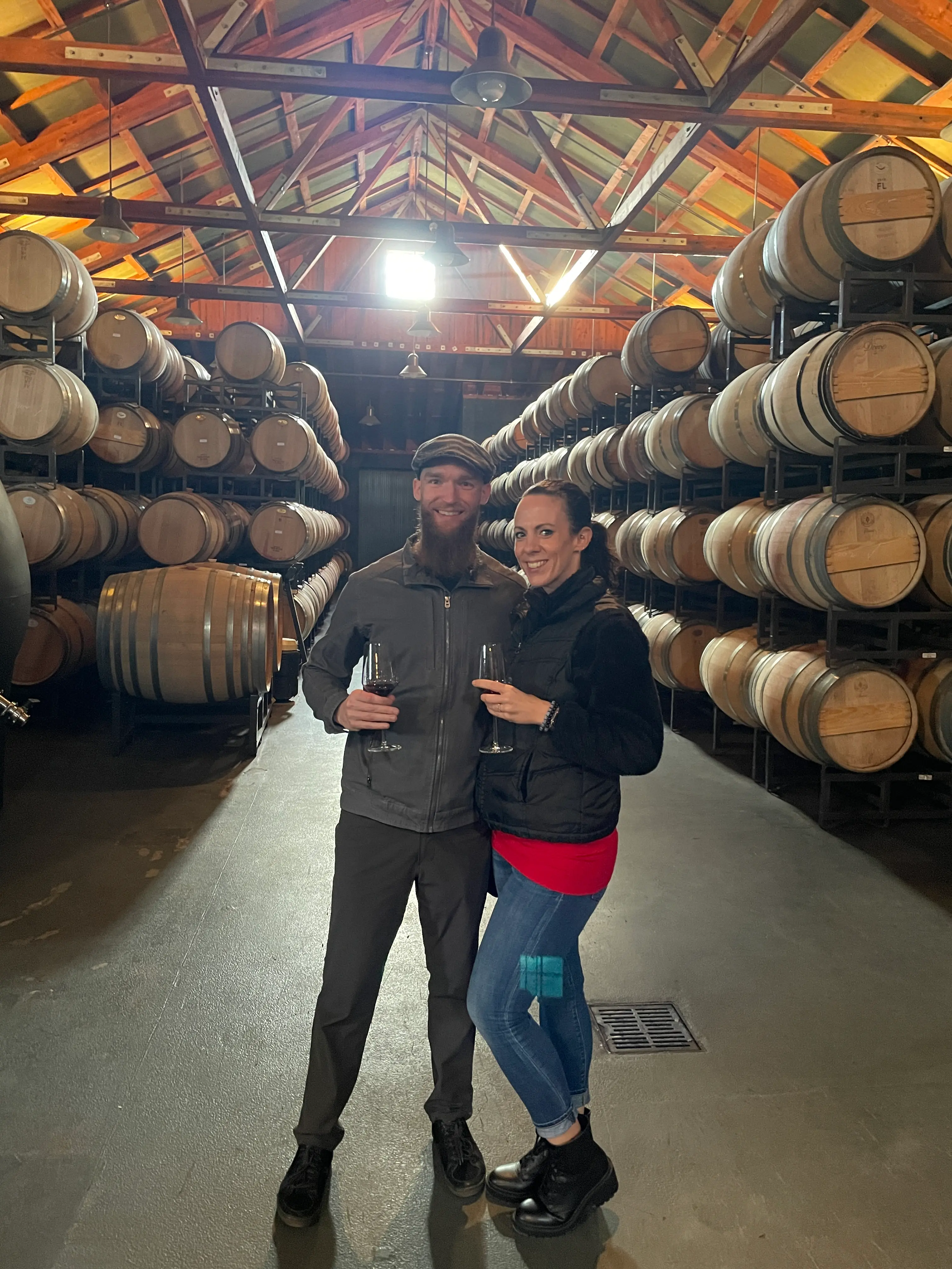 Dr. Matt with his wife holding wine in warehouse full of wine barrels