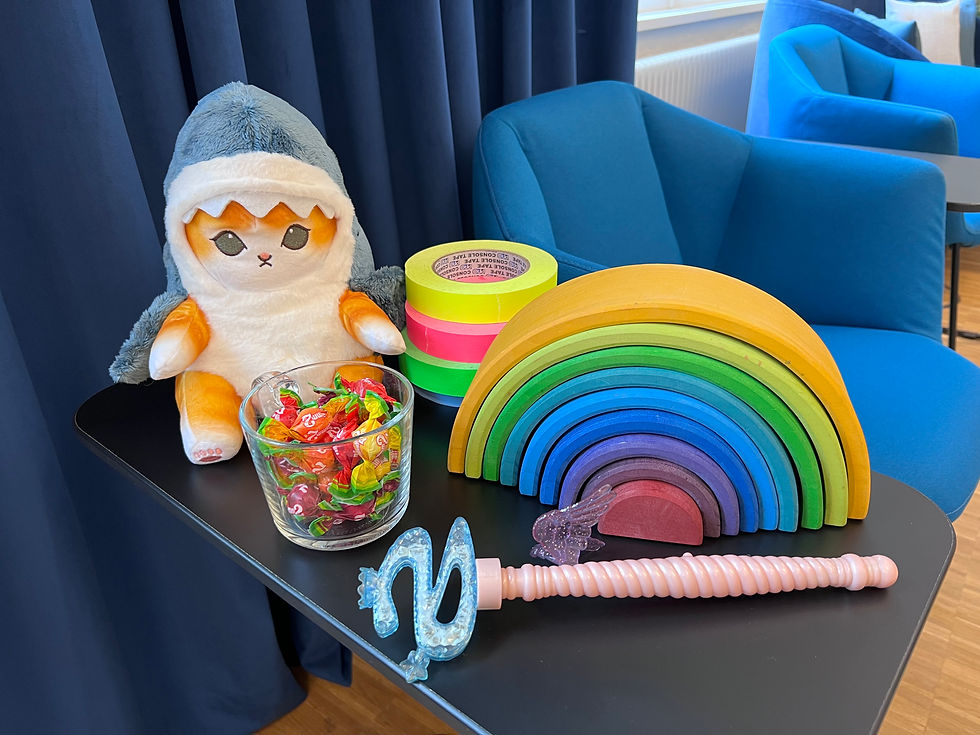 Trainingsrequisiten auf einem Tisch: Plastik-Zauberstab, Katzenkuscheltier in Hai-Verkleidung, buntes Klebeband, ein glas mit bunten Kaubonbons.